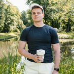 Casual young man in a park, holding a coffee cup. Sunny day in nature.