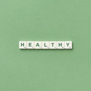 Scrabble tiles spelling the word 'healthy' on a light green background, top view.